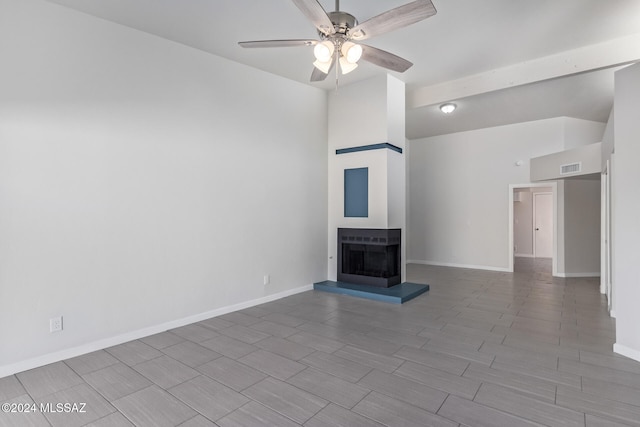 unfurnished living room with ceiling fan, a towering ceiling, a multi sided fireplace, and hardwood / wood-style floors