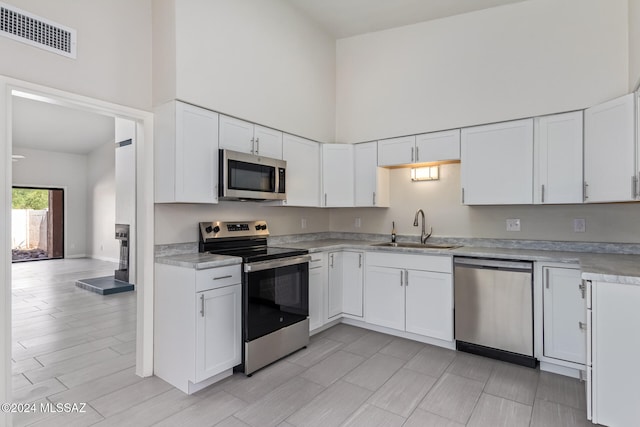 kitchen with white cabinets, light wood-type flooring, sink, a towering ceiling, and stainless steel appliances