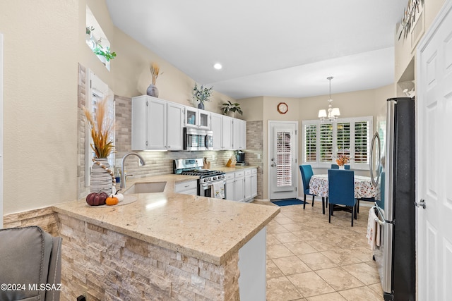 kitchen featuring kitchen peninsula, white cabinetry, stainless steel appliances, pendant lighting, and light stone counters