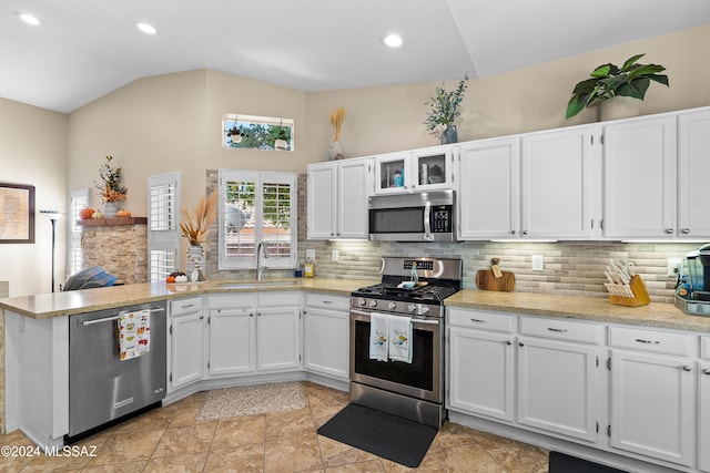 kitchen with kitchen peninsula, backsplash, sink, white cabinetry, and appliances with stainless steel finishes