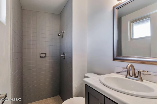 full bathroom featuring toilet, tiled shower, and vanity