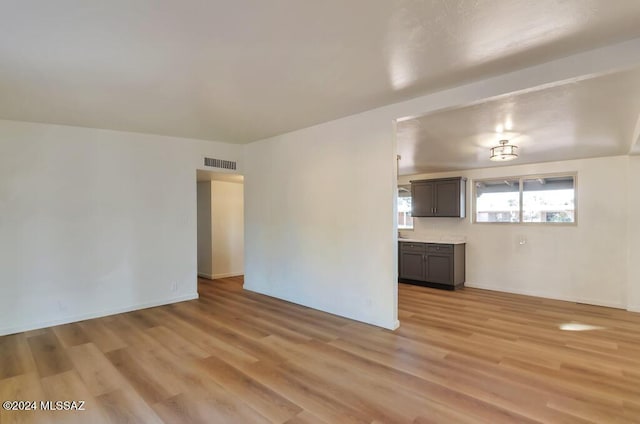 unfurnished living room featuring visible vents, light wood finished floors, and baseboards