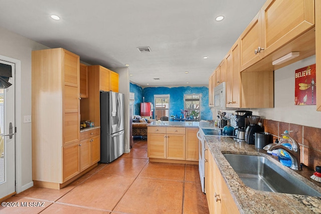 kitchen featuring sink, stainless steel refrigerator with ice dispenser, light brown cabinetry, light tile patterned floors, and range