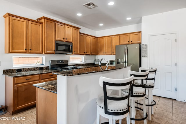 kitchen with appliances with stainless steel finishes, dark stone counters, a kitchen island with sink, a breakfast bar area, and light tile patterned flooring