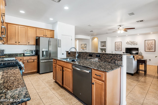 kitchen with a kitchen island with sink, dark stone counters, sink, ceiling fan, and stainless steel appliances