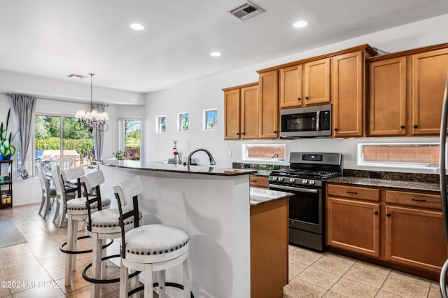 kitchen with dark stone counters, stainless steel appliances, pendant lighting, a center island with sink, and a chandelier