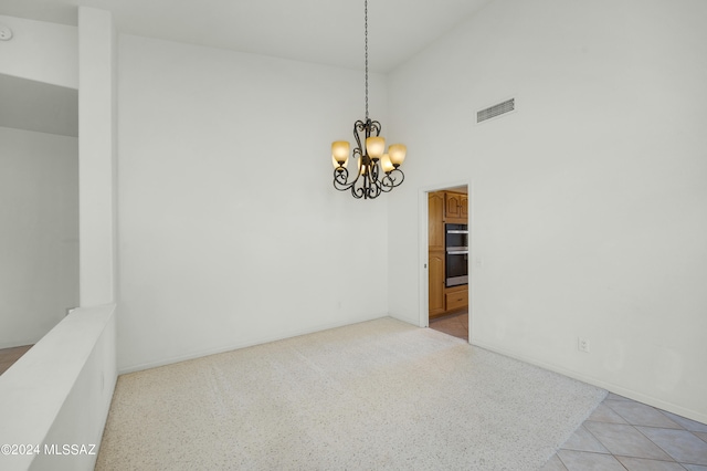 tiled empty room featuring a chandelier and a high ceiling