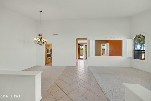 spare room with a towering ceiling, an inviting chandelier, light colored carpet, and plenty of natural light