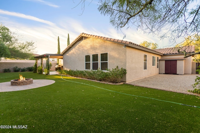 back of property with a shed, a patio area, a fire pit, and a yard