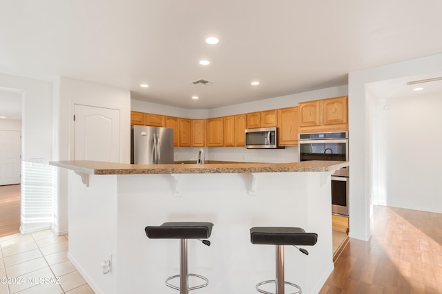 kitchen with light hardwood / wood-style floors, stainless steel appliances, a kitchen bar, and an island with sink