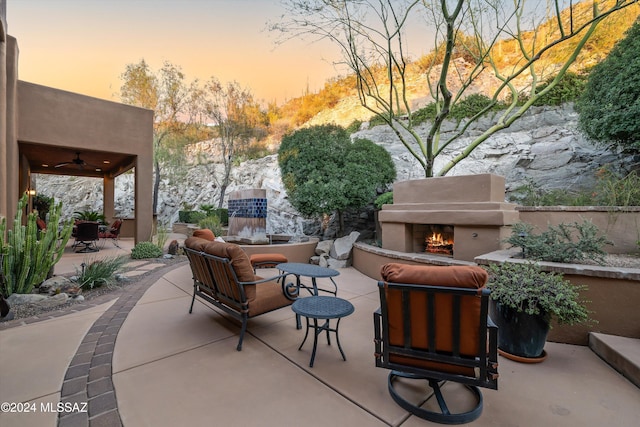 patio terrace at dusk featuring an outdoor living space with a fireplace and ceiling fan