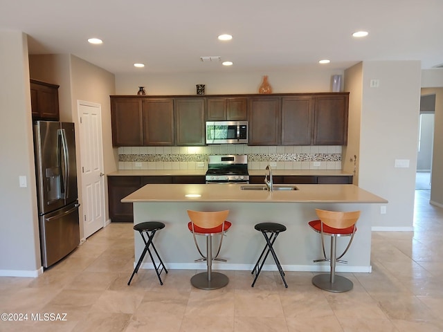 kitchen with tasteful backsplash, appliances with stainless steel finishes, sink, a kitchen breakfast bar, and a center island with sink