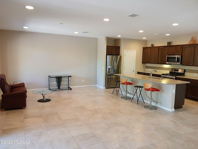 kitchen with tasteful backsplash, appliances with stainless steel finishes, dark brown cabinets, a breakfast bar area, and a center island with sink