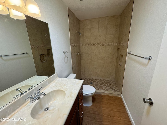 bathroom with tiled shower, toilet, hardwood / wood-style floors, vanity, and a textured ceiling