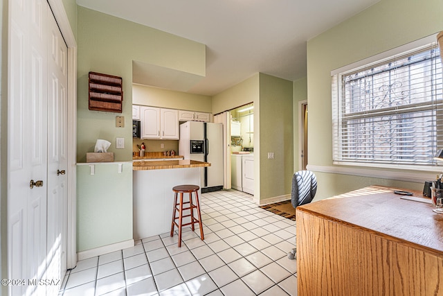 kitchen with a kitchen breakfast bar, light tile patterned flooring, white refrigerator with ice dispenser, kitchen peninsula, and white cabinets