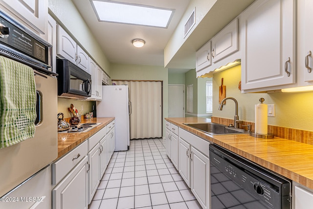 kitchen featuring black appliances, sink, a skylight, light tile patterned flooring, and white cabinetry