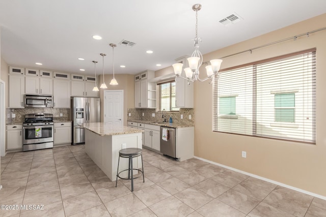 kitchen with a kitchen island, appliances with stainless steel finishes, sink, hanging light fixtures, and light stone counters