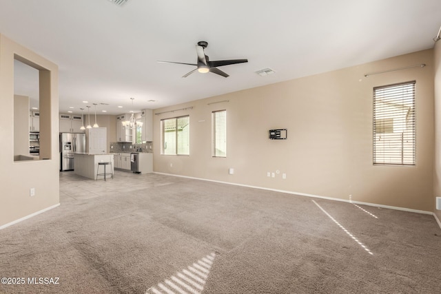 unfurnished living room with ceiling fan with notable chandelier and light carpet