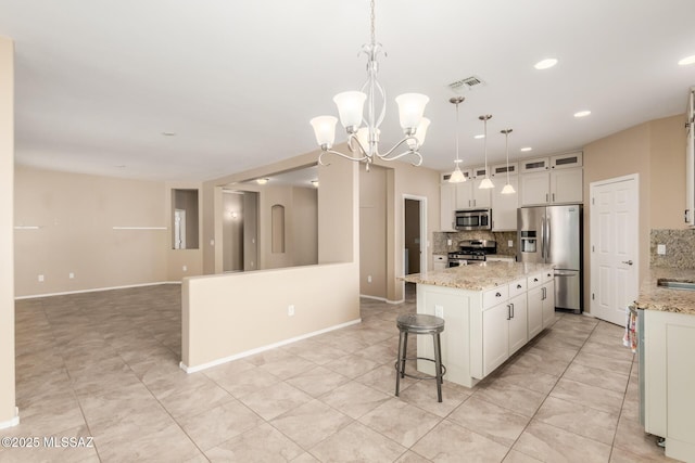 kitchen featuring appliances with stainless steel finishes, decorative light fixtures, white cabinetry, a center island, and light stone countertops