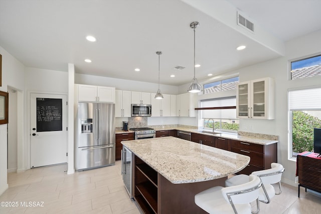 kitchen with a kitchen island, a sink, appliances with stainless steel finishes, open shelves, and glass insert cabinets