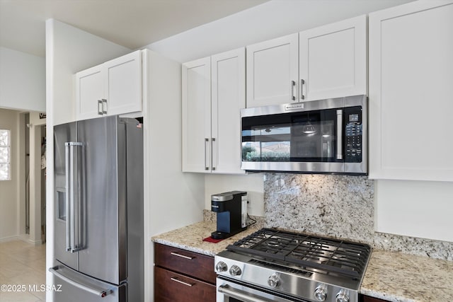 kitchen featuring appliances with stainless steel finishes, white cabinets, light stone counters, and tasteful backsplash