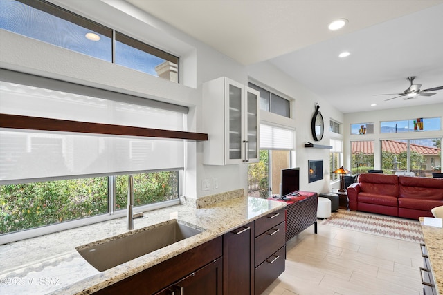 kitchen featuring a sink, dark brown cabinets, light stone countertops, a glass covered fireplace, and glass insert cabinets