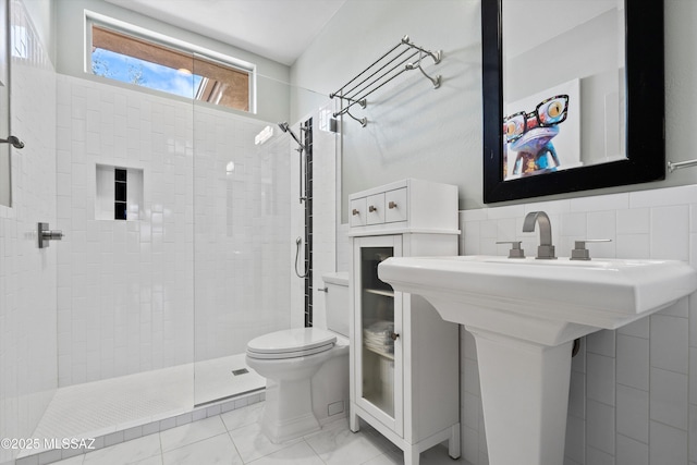 full bath featuring a sink, a tile shower, toilet, and tile walls