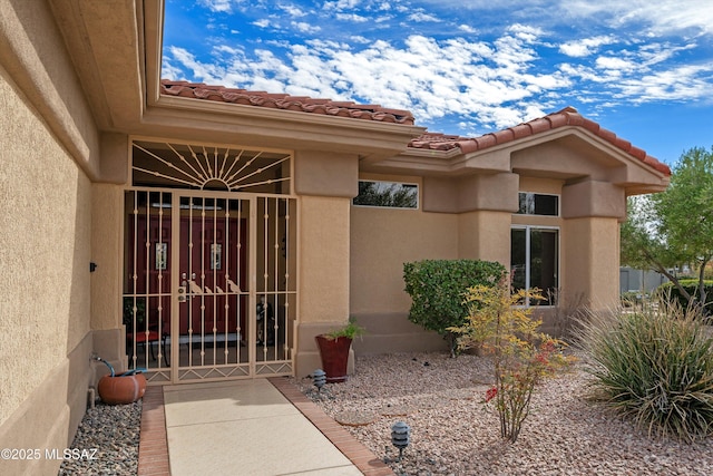 doorway to property featuring a gate, a tile roof, and stucco siding