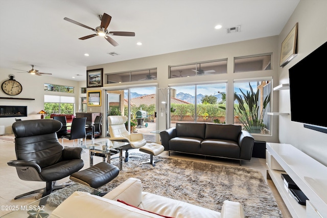 living room featuring a ceiling fan, a glass covered fireplace, visible vents, and recessed lighting