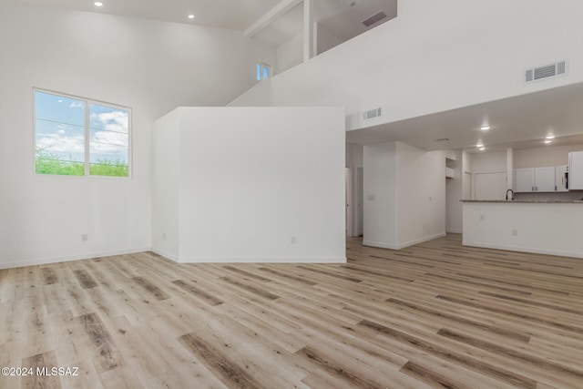 unfurnished living room with light wood-type flooring and high vaulted ceiling