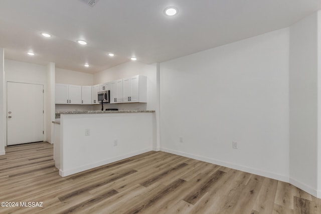 kitchen with white cabinetry, light stone countertops, light hardwood / wood-style flooring, and kitchen peninsula