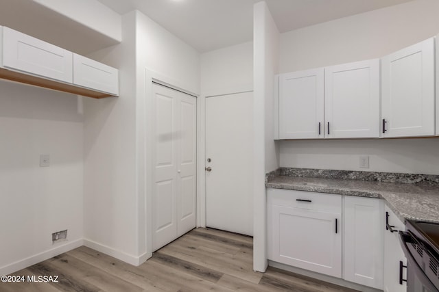 kitchen with white cabinetry, stainless steel range oven, light wood-type flooring, and dark stone countertops