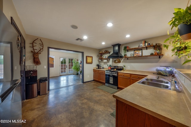 kitchen featuring french doors, stainless steel gas stove, sink, wall chimney range hood, and concrete floors