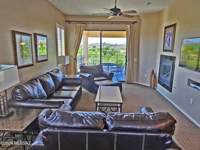 living room with a tiled fireplace, carpet flooring, a ceiling fan, and baseboards