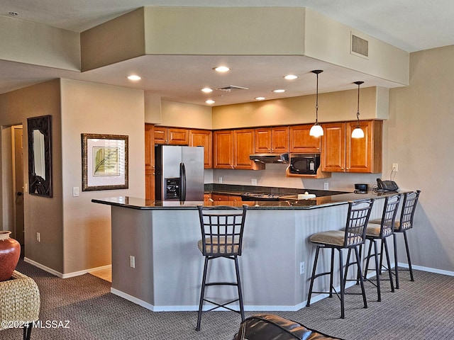 kitchen featuring black microwave, under cabinet range hood, a peninsula, stainless steel fridge with ice dispenser, and brown cabinets