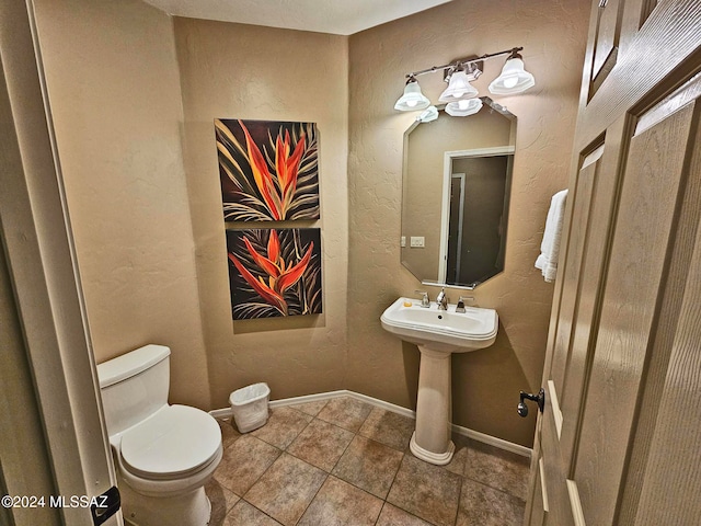 half bath featuring a textured wall, tile patterned floors, toilet, and baseboards