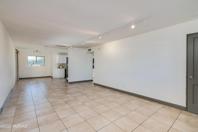 empty room featuring a textured ceiling, track lighting, and light tile patterned flooring