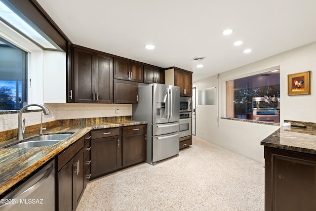 kitchen with dark brown cabinets, stainless steel appliances, dark stone counters, and sink