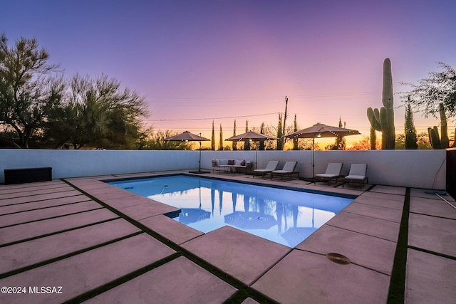 pool at dusk featuring a fenced in pool, a patio area, and fence