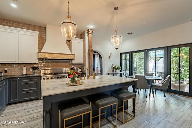 kitchen featuring custom exhaust hood, stove, white cabinets, light stone counters, and backsplash