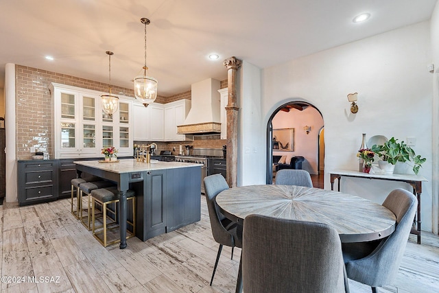 kitchen featuring a kitchen island with sink, stainless steel stove, premium range hood, tasteful backsplash, and arched walkways