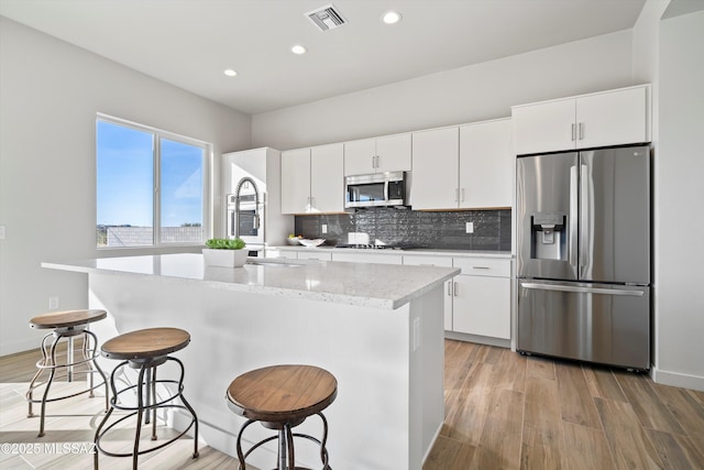 kitchen featuring visible vents, stainless steel appliances, a kitchen island with sink, and white cabinetry