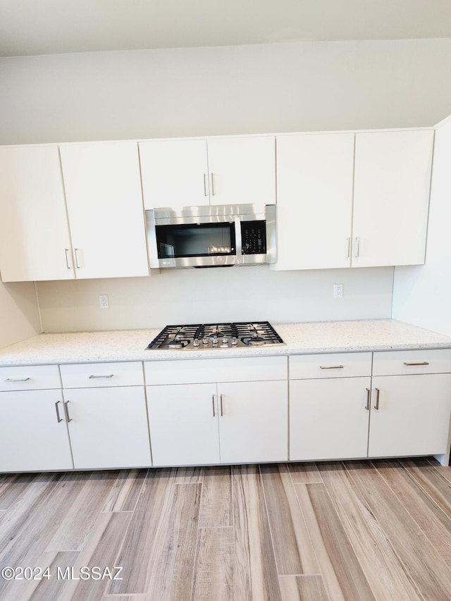 kitchen featuring white cabinetry, stainless steel appliances, light stone counters, and light wood-type flooring