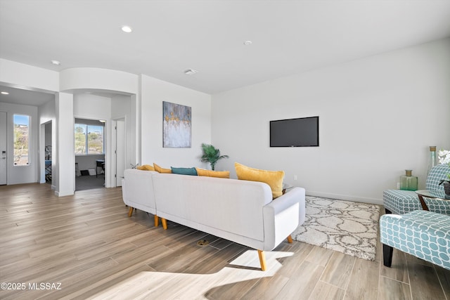 living room featuring light wood-type flooring, baseboards, arched walkways, and recessed lighting