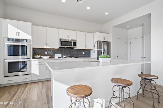 kitchen with a kitchen island with sink, stainless steel appliances, a breakfast bar, and white cabinetry