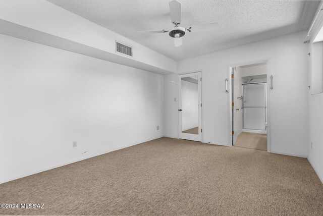 unfurnished bedroom featuring a walk in closet, a textured ceiling, a closet, ceiling fan, and light carpet