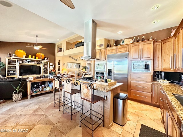 kitchen with built in appliances, a kitchen island, light stone counters, island range hood, and a kitchen bar