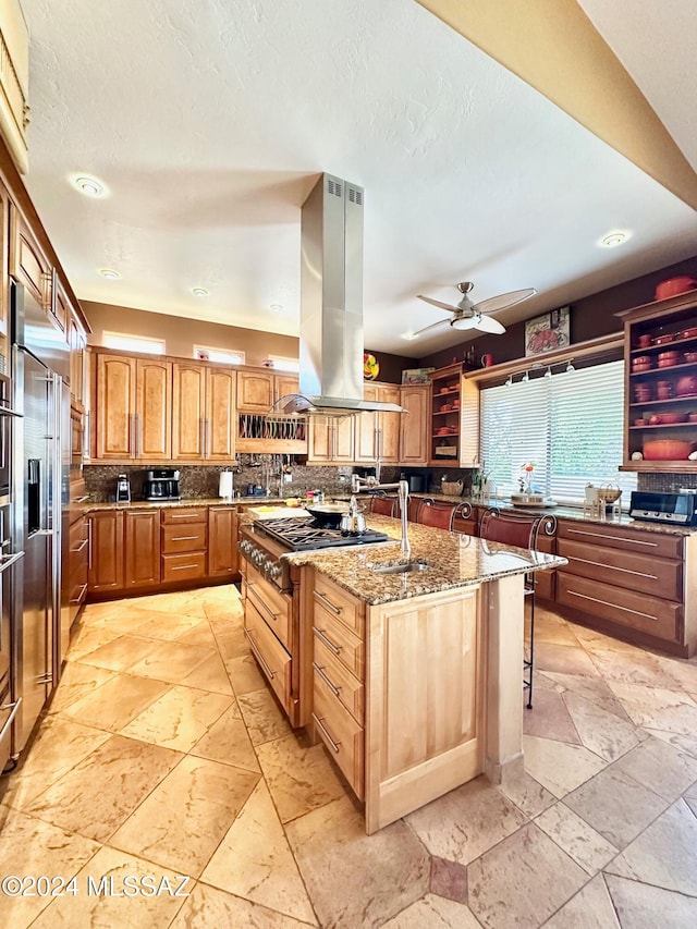 kitchen with light stone counters, a breakfast bar area, decorative backsplash, a center island with sink, and island range hood