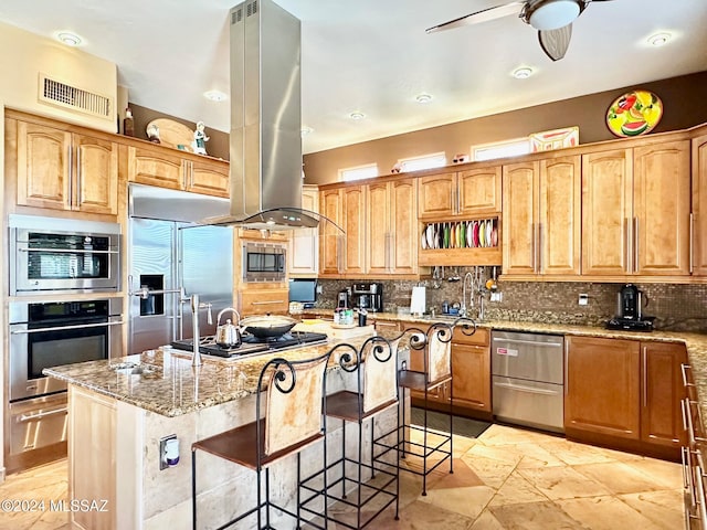 kitchen featuring island exhaust hood, built in appliances, light stone counters, and an island with sink