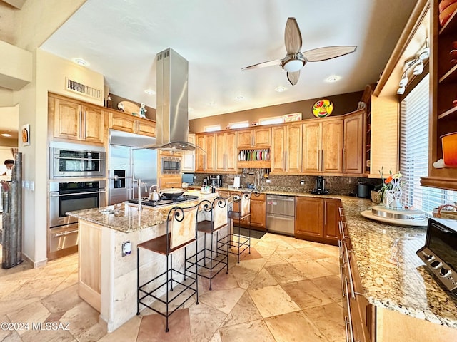 kitchen featuring island exhaust hood, a kitchen bar, decorative backsplash, built in appliances, and a center island with sink